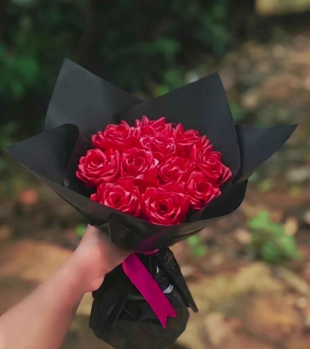 A bouquet of red roses wrapped in black with a pink ribbon